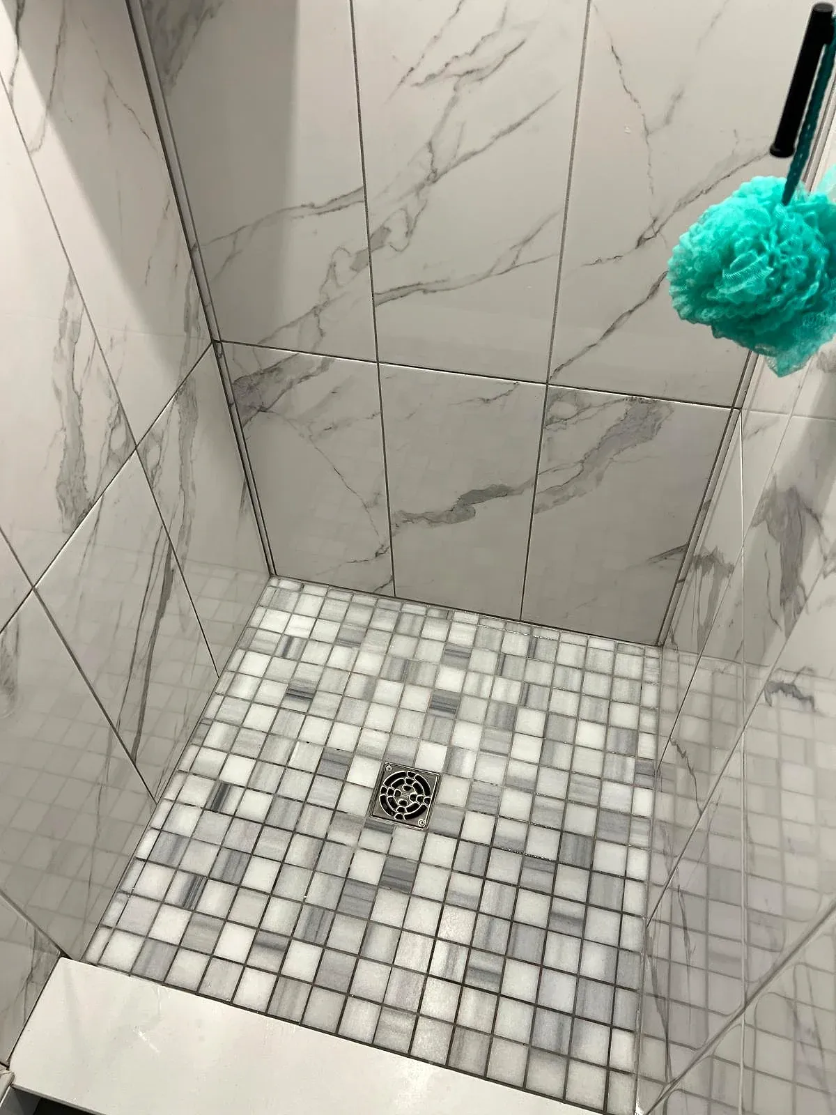A tiled shower with clean marble-look walls, mosaic floor and drain.