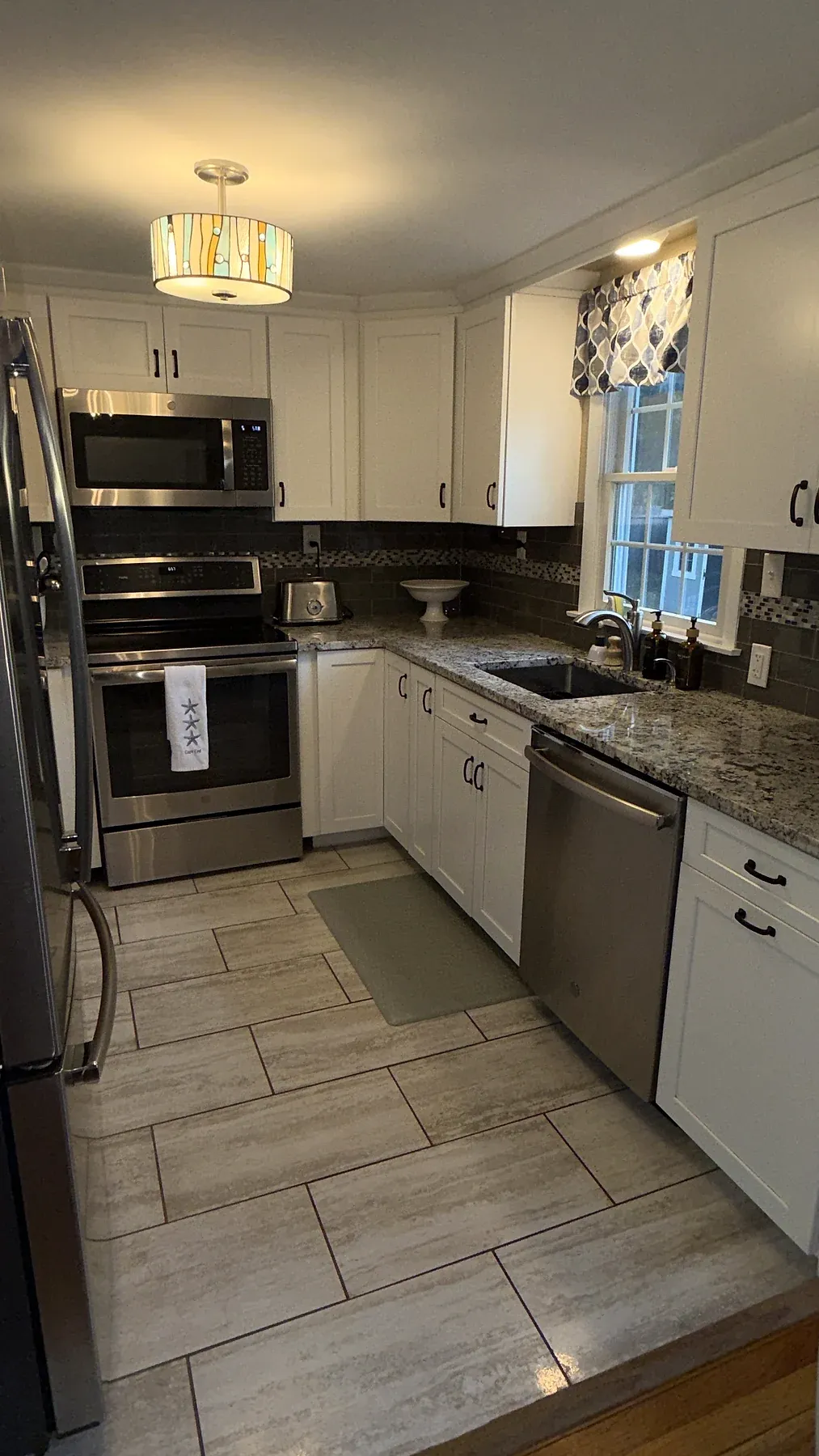 A clean residential kitchen with white cabinets, stone counters and stainless appliances.